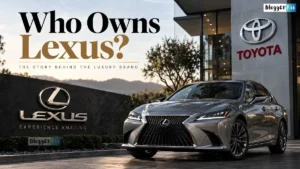 A silver Lexus sedan parked outside a modern Toyota building, with the headline “Who Owns Lexus?” and Lexus branding prominently displayed.